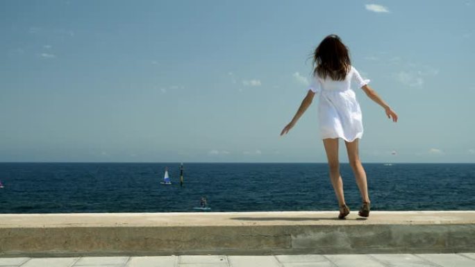 巴塞罗那港。在地中海边的一个码头上，一个穿着白色连衣裙的美女从一侧跳到另一侧。西班牙。4K