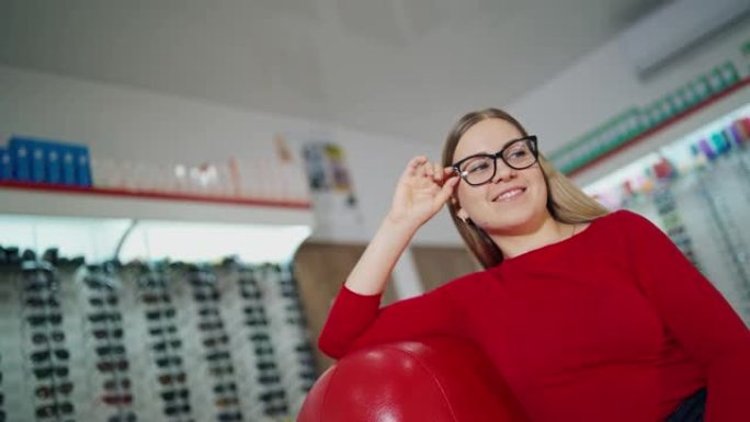 穿着时尚眼镜的美女。女顾客坐在扶手椅上，在眼镜店试戴新眼镜。眼镜概念。