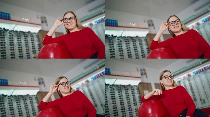 穿着时尚眼镜的美女。女顾客坐在扶手椅上，在眼镜店试戴新眼镜。眼镜概念。