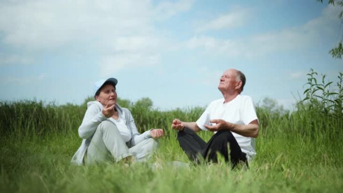 健康的生活方式在老年，一对热爱运动生活方式的已婚老年夫妇在户外进行体育锻炼坐在温暖的阳光明媚的绿色草