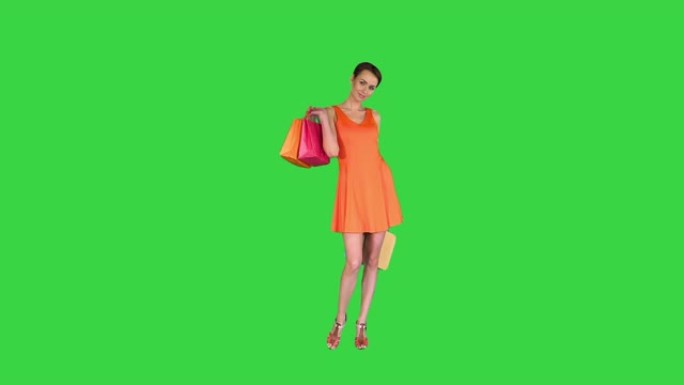 美丽的女孩在绿色屏幕上显示带有购买商品的包，色度键