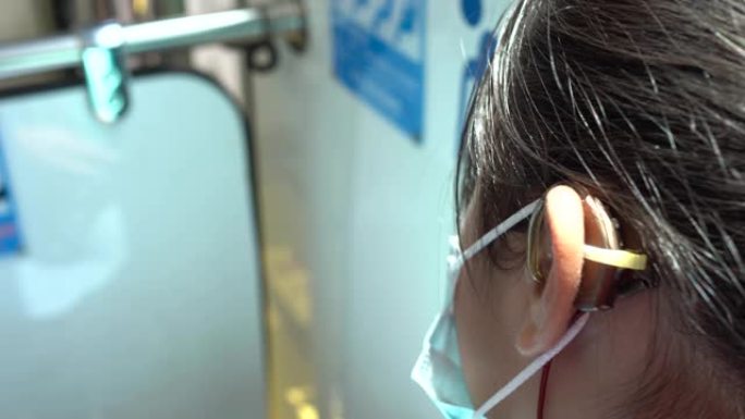 坐在公共汽车上的听力损失女孩。重点是助听器。模糊的背景是兄弟会席位的象征，包括孕妇、老人、残疾人。