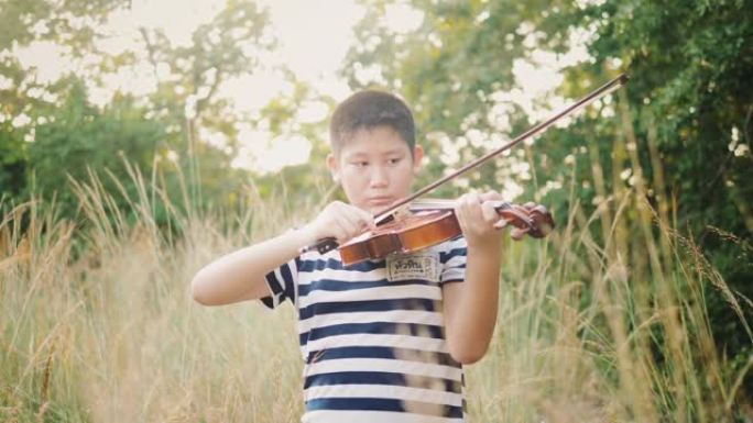 亚洲青春期男孩在草地上用阳光拉小提琴，慢动作。