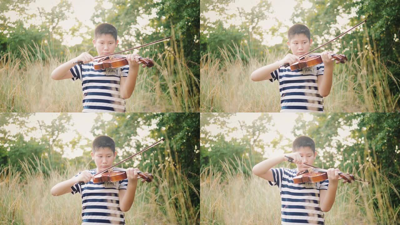 亚洲青春期男孩在草地上用阳光拉小提琴，慢动作。