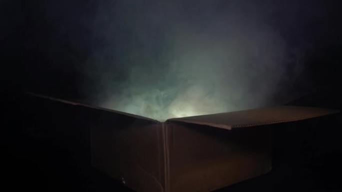 一名男子打开一个纸板箱，从中冒出烟雾，并发出多色的光芒。魔法和魔法的概念，惊喜