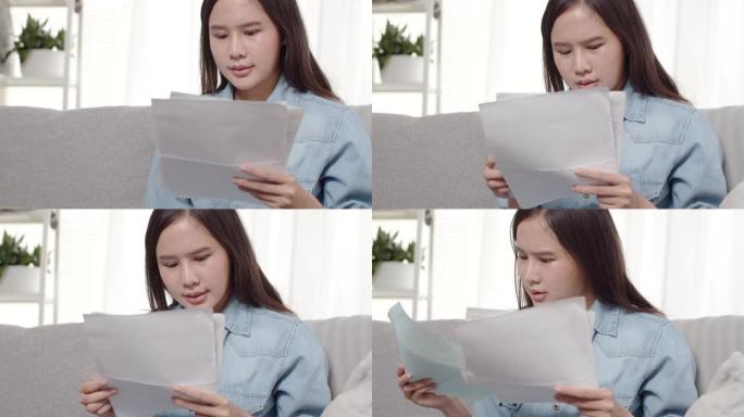 沮丧的年轻亚洲妇女坐在家里的沙发上，拿着过期的账单和信用卡。。
