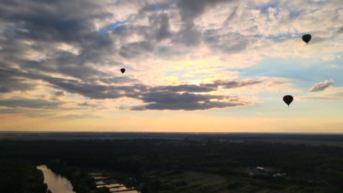 夏季日落时，在多云的蓝天中，热气球在欧洲小城市附近的乡村上空飞行的剪影，空中4k视图
