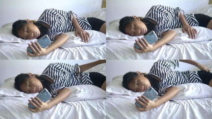 快乐的亚洲女孩使用智能手机和躺在床上在家里，生活方式的概念。
