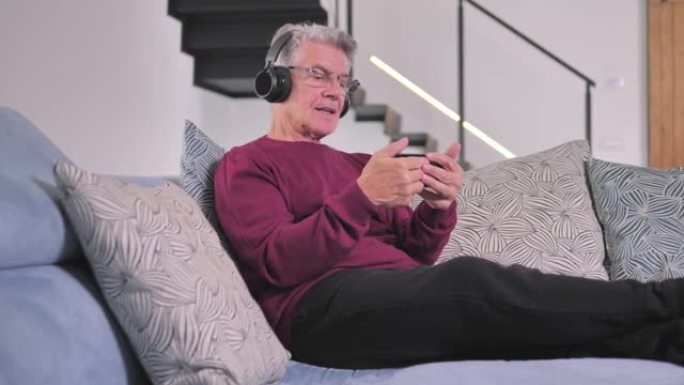 沙发上戴着耳机的老人通过蓝牙智能手机听音乐