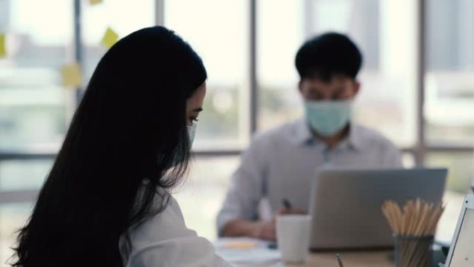 医疗标志的亚洲商人手持便条纸会议与新的创业项目分享给业务团队。一群工人坐在桌子旁听演讲者。商务会议概