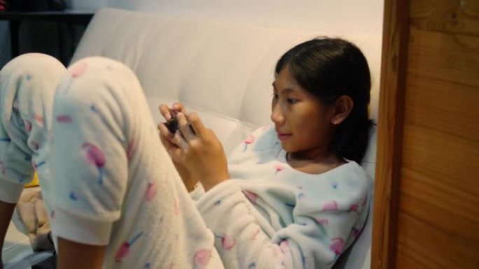 快乐的亚洲女孩在晚上在家的智能手机上玩网络游戏，生活方式概念。