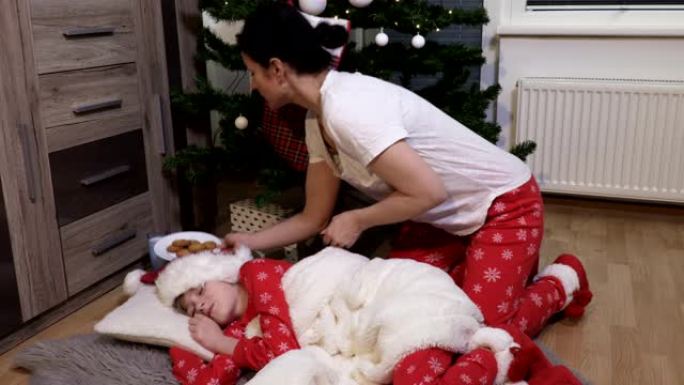 圣诞睡衣中的女人在圣诞树下为圣诞老人放牛奶和饼干