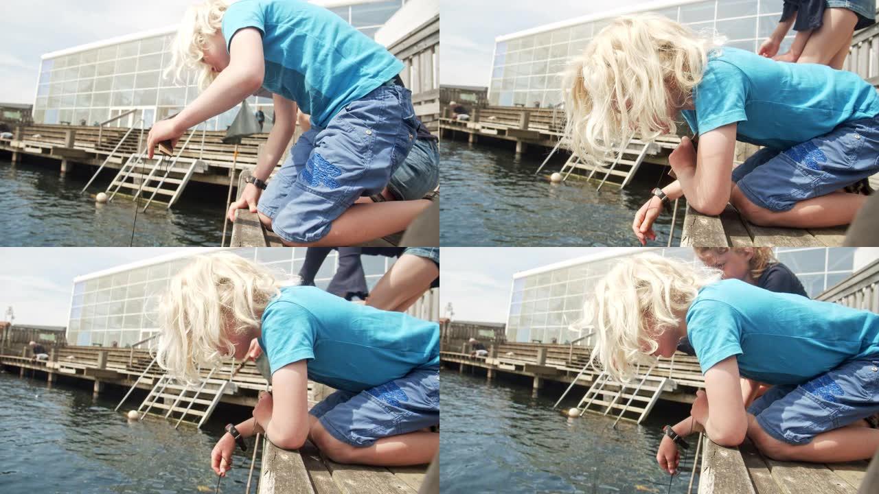 码头边缘的兄弟姐妹俯身用绳子抓螃蟹