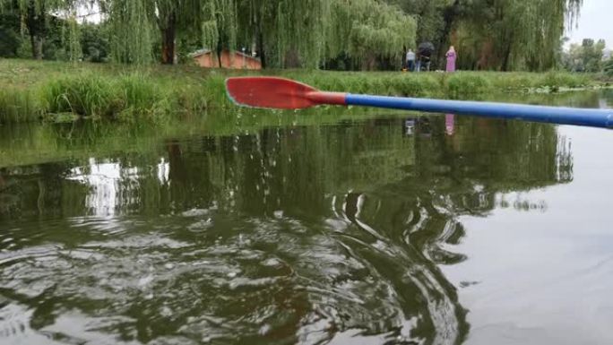 在水中划桨。公园里的塑料桨特写，背景是湖和睡莲。蓝色塑料桨划过水面。红色和蓝色桨特写。水滴向下流动