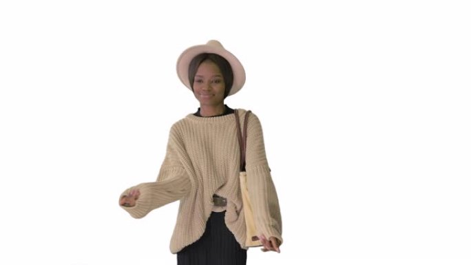 穿着针织品和白帽子的时尚非洲裔美国女性在白色背景上行走时跳舞