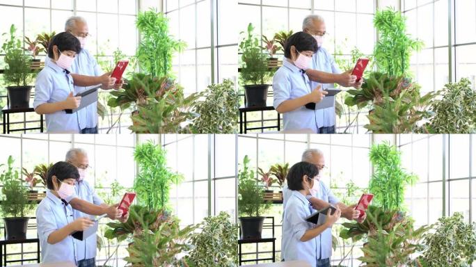 亚洲退休的祖父和孙子戴着口罩，在有趣的平板电脑上出售植物。退休爱好和生活方式。老人和年轻人之间的家庭
