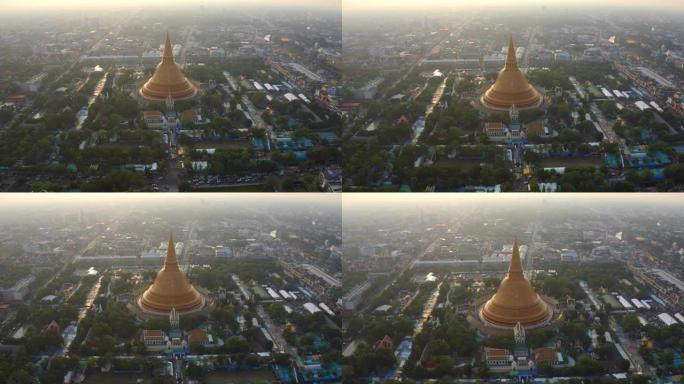 日落时Phra Pathommachedi寺的空中俯视图。带有民居的金色佛教宝塔，泰国纳康帕通区城市