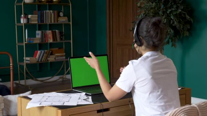 一名年轻的印度妇女使用带有绿屏的笔记本电脑进行在线电话会议，与人一起培训，在家中明亮的房间