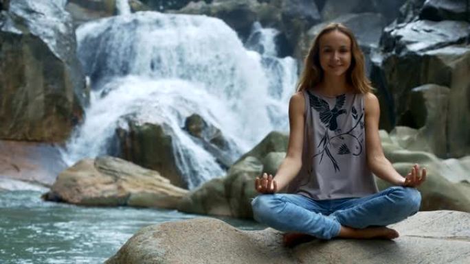 微笑的长发女孩在瀑布附近做瑜伽