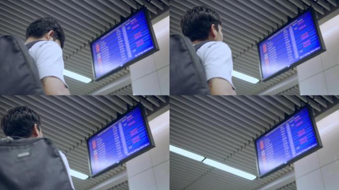 亚洲青年男子在机场用智能手机检查出发板
