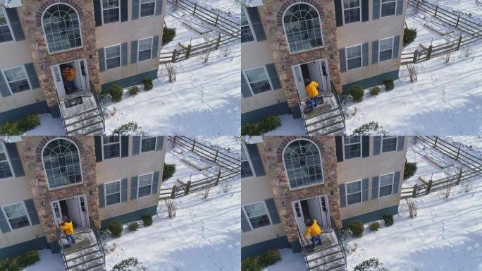 一名50岁的成年长发男子穿着黄色外套，在冬季降雪后，他从雪地上清理了乡间别墅前院的小路后返回家中。