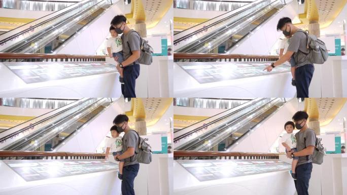 亚洲爸爸戴防护口罩抱男婴在商场看地图