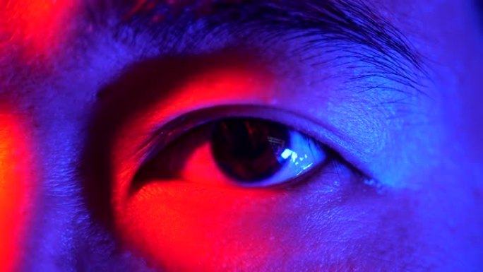 在五颜六色的霓虹灯下睁开眼睛的人的脸。男人眼睛的特写