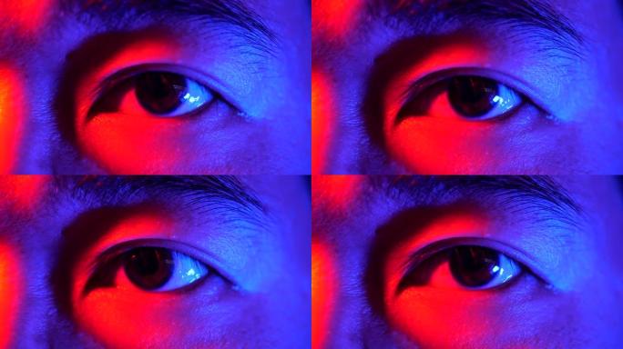在五颜六色的霓虹灯下睁开眼睛的人的脸。男人眼睛的特写