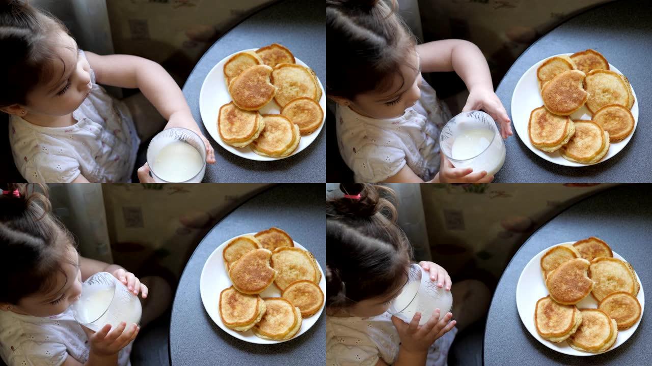 可爱的小女孩在厨房的桌子上用手吃起司蛋糕。桌上有一杯酸奶