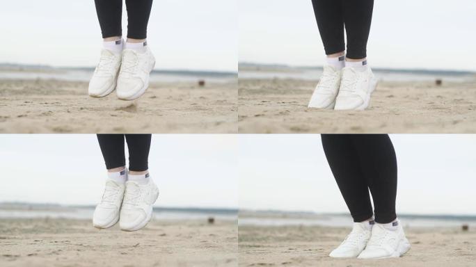 一个穿着白色运动鞋的女孩在沙滩上跳绳。特写腿。海滩上夏天阴天。
