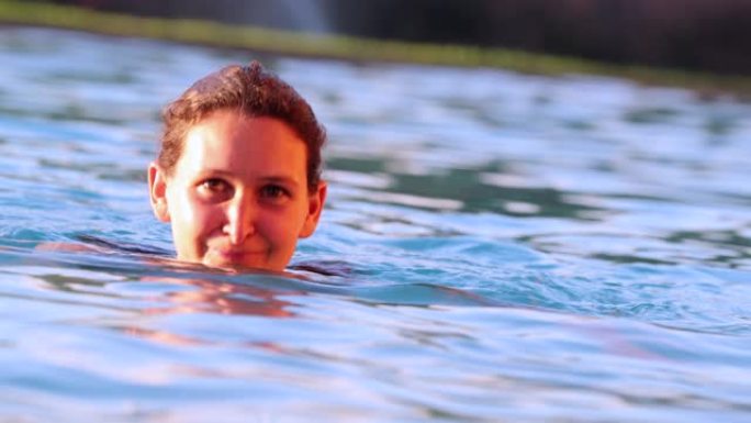 魅力四射的有趣女人在游泳池水中游泳时对着镜头微笑
