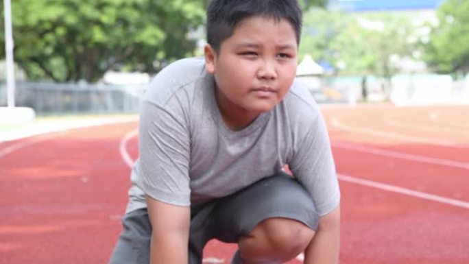 健康和自信的胖男孩在开始的位置准备跑步。儿童运动员即将开始冲刺。锻炼概念