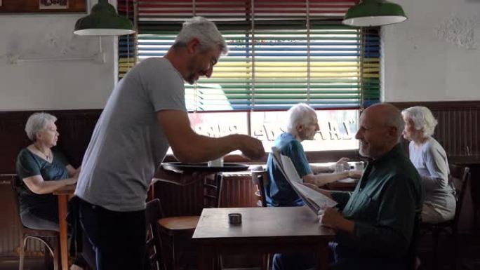 高加索服务员为在咖啡馆里读报纸的成年男子提供咖啡馆