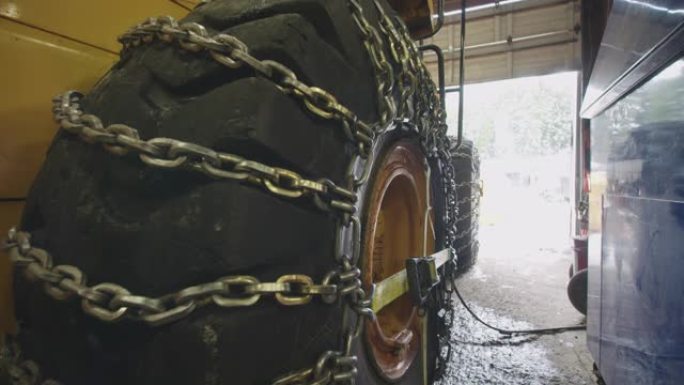 黄色工业建筑车辆在工作车间用冬季防滑链封闭在巨大的轮胎上