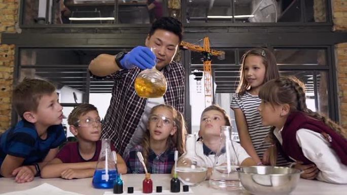科学家向孩子们展示如何在实验课上进行化学反应实验。玻璃烧瓶中的化学反应橙色。科学、化学和科学家