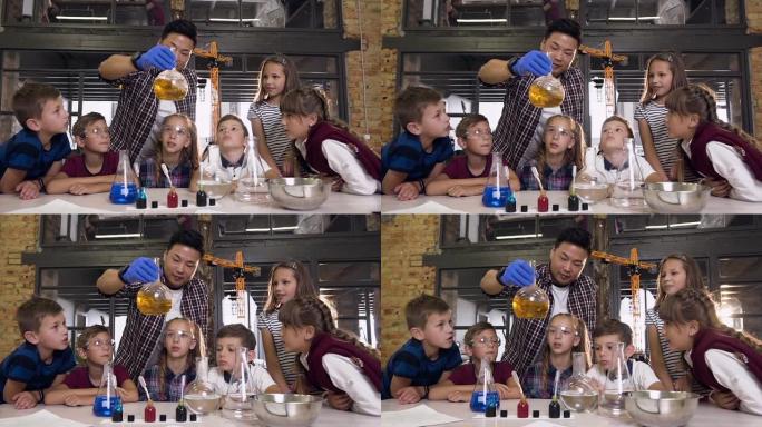 科学家向孩子们展示如何在实验课上进行化学反应实验。玻璃烧瓶中的化学反应橙色。科学、化学和科学家