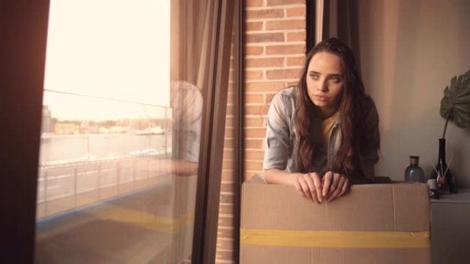 沮丧孤独的年轻女性透过窗户看的肖像。焦虑女孩看着房子或酒店房间。在电晕病毒新型冠状病毒肺炎期间由于社