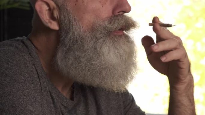 一个留着胡子的白发老人在厨房里抽烟。特写