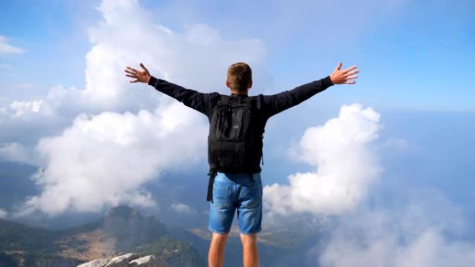 背包的徒步旅行者站在山边，举起双手享受自由。人在探索新地方的旅行中积极休息。游客欣赏山顶风景。多莉开