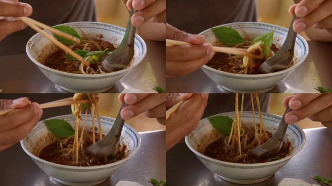 吃着面条，这个人用筷子和勺子把面条舀在杯子里，慢慢举到嘴里。