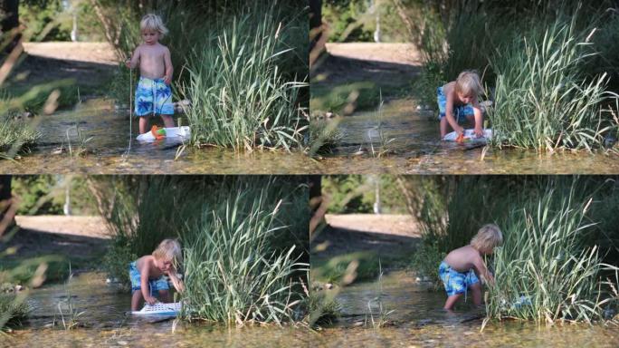 可爱的金发孩子，蹒跚学步的男孩在河上玩塑料船，夏天