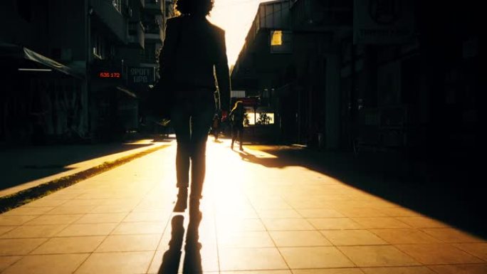 剪影女人在充满活力的日出时走在现代城市的人行道上