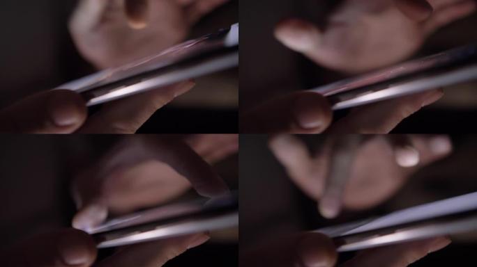 男人在黑暗中使用手机，滚动屏幕，放大屏幕上的图片，特写