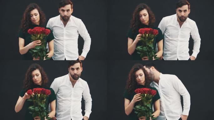可爱的女孩很难过，因为一朵红玫瑰坏了。站在她这边的男人行为愚蠢，做鬼脸。