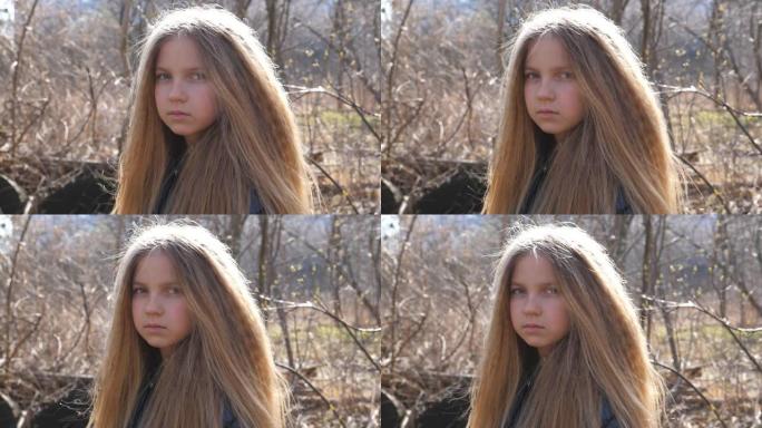 初春森林模糊背景下绝望的孩子的肖像。金发小女孩在户外看着相机。小孩子女性脸上悲伤的表情。特写