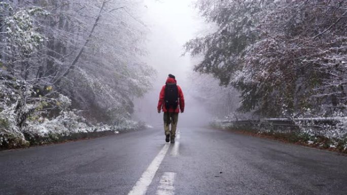 男游客背着黑色大背包在柏油路上行走，在冬天四处张望。失去了概念