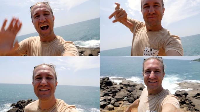 一个有趣的年轻人在悬崖上拍自拍视频，他在海边挥手打招呼，还做了沙卡手势。人们在网上分享度假的概念