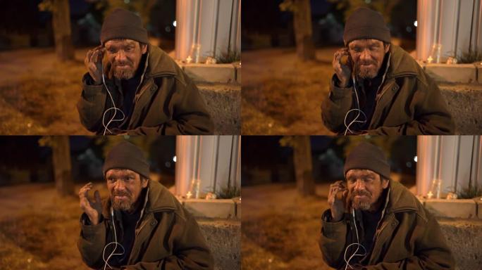 无家可归的人晚上坐在街上使用耳机。
