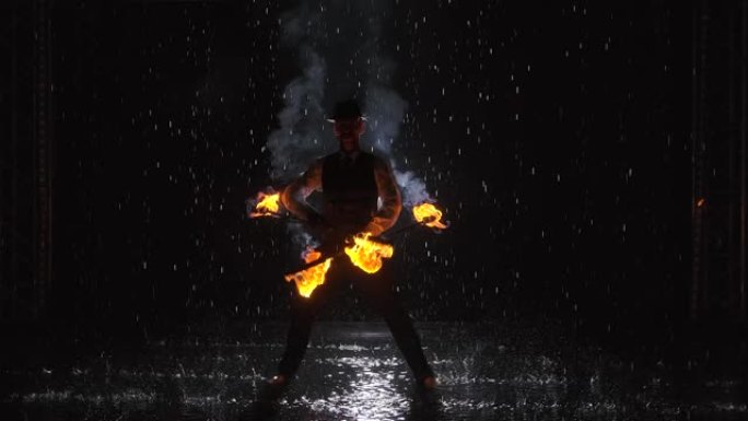 一个男人在雨中在黑暗的工作室里做专业消防表演的剪影。慢动作