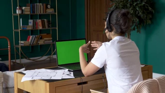 坐在椅子上的年轻女子在带有绿色模拟屏幕的笔记本电脑上工作。女孩使用电脑，在线电话会议，与人一起培训，